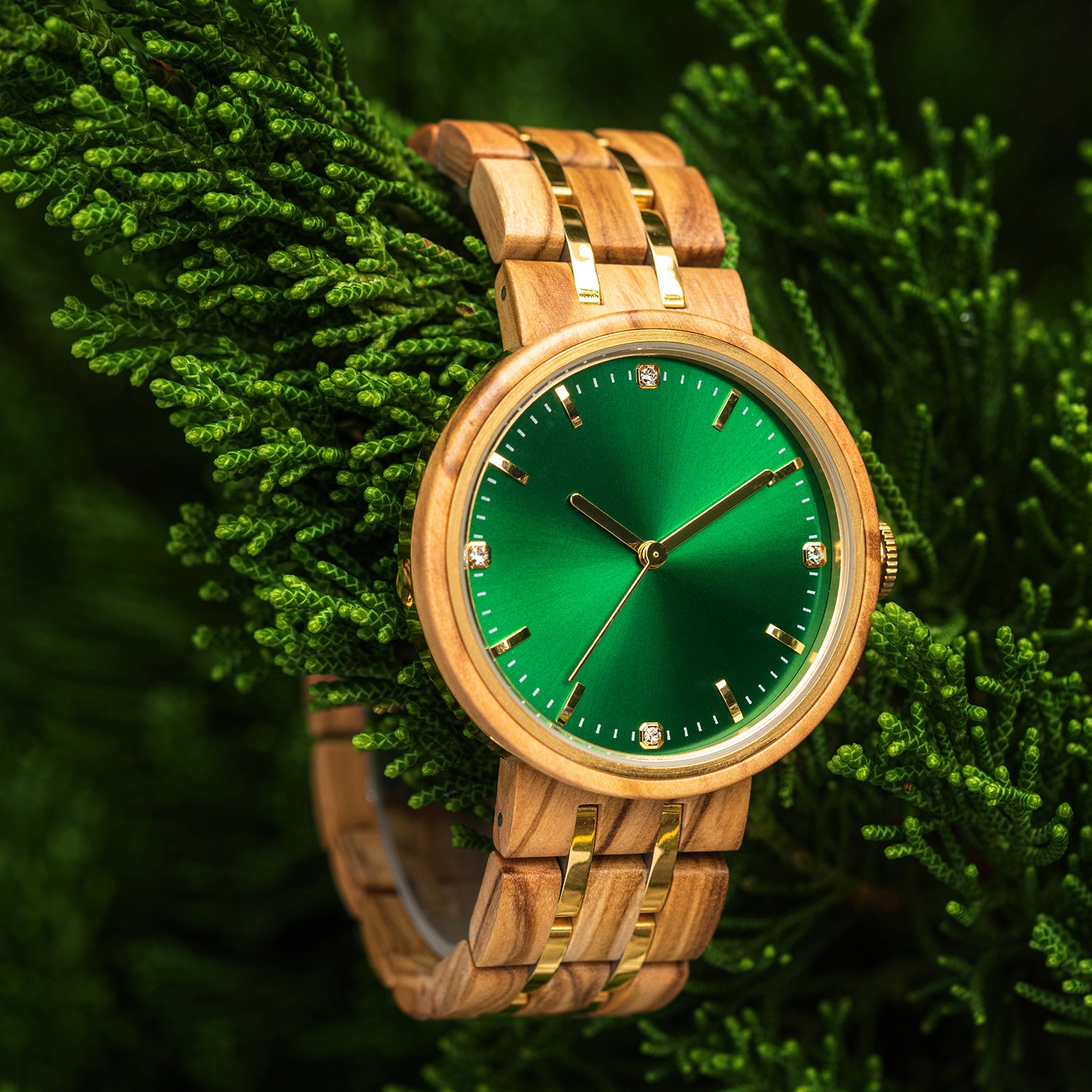 An elegant women's wooden watch featuring a green dial, gold-tone accents, diamond-like details, and a two-tone wood and metal band, nestled amidst green foliage to highlight its luxurious and natural design.