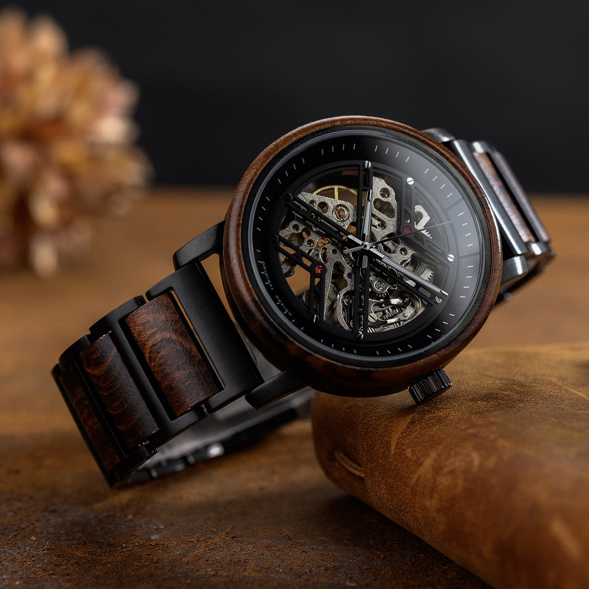 A men's skeleton mechanical watch with a wooden and black metal case and band, showcasing intricate internal mechanisms through a black dial, positioned on a brown leather surface with a rustic background.
