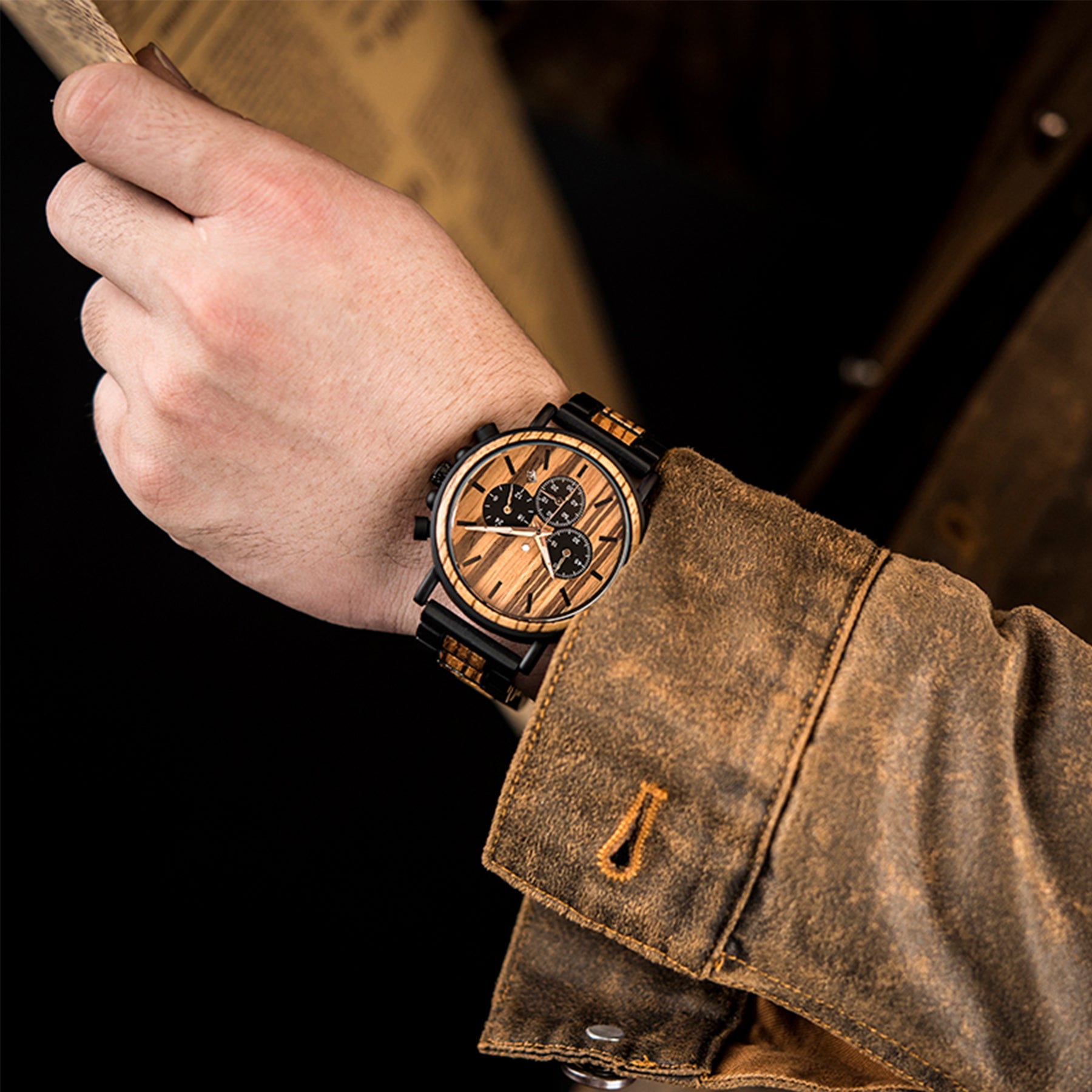 A man wearing a black metal and zebrawood chronograph watch with zebrawood face